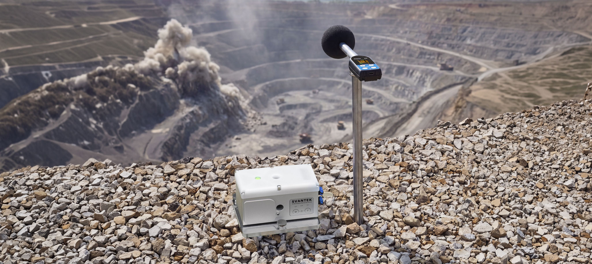 SV 810 air-overpressure meter on a pole beside an SV 804 vibration monitor, installed on the rim of an open-pit mine during a production blast