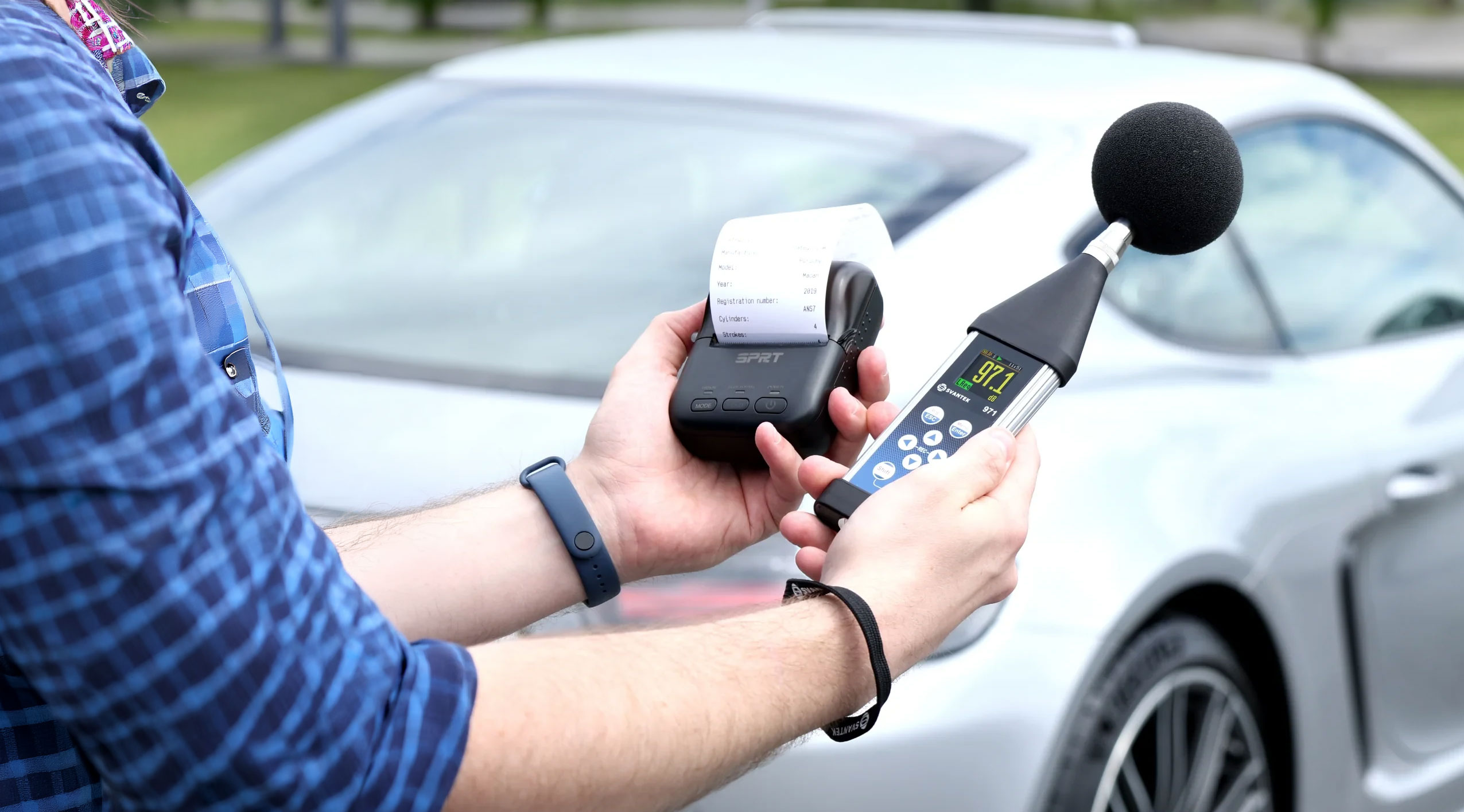 Operator measuring vehicle noise with an SV 971A Class 1 sound level meter and an SP 74 wireless printer beside a car